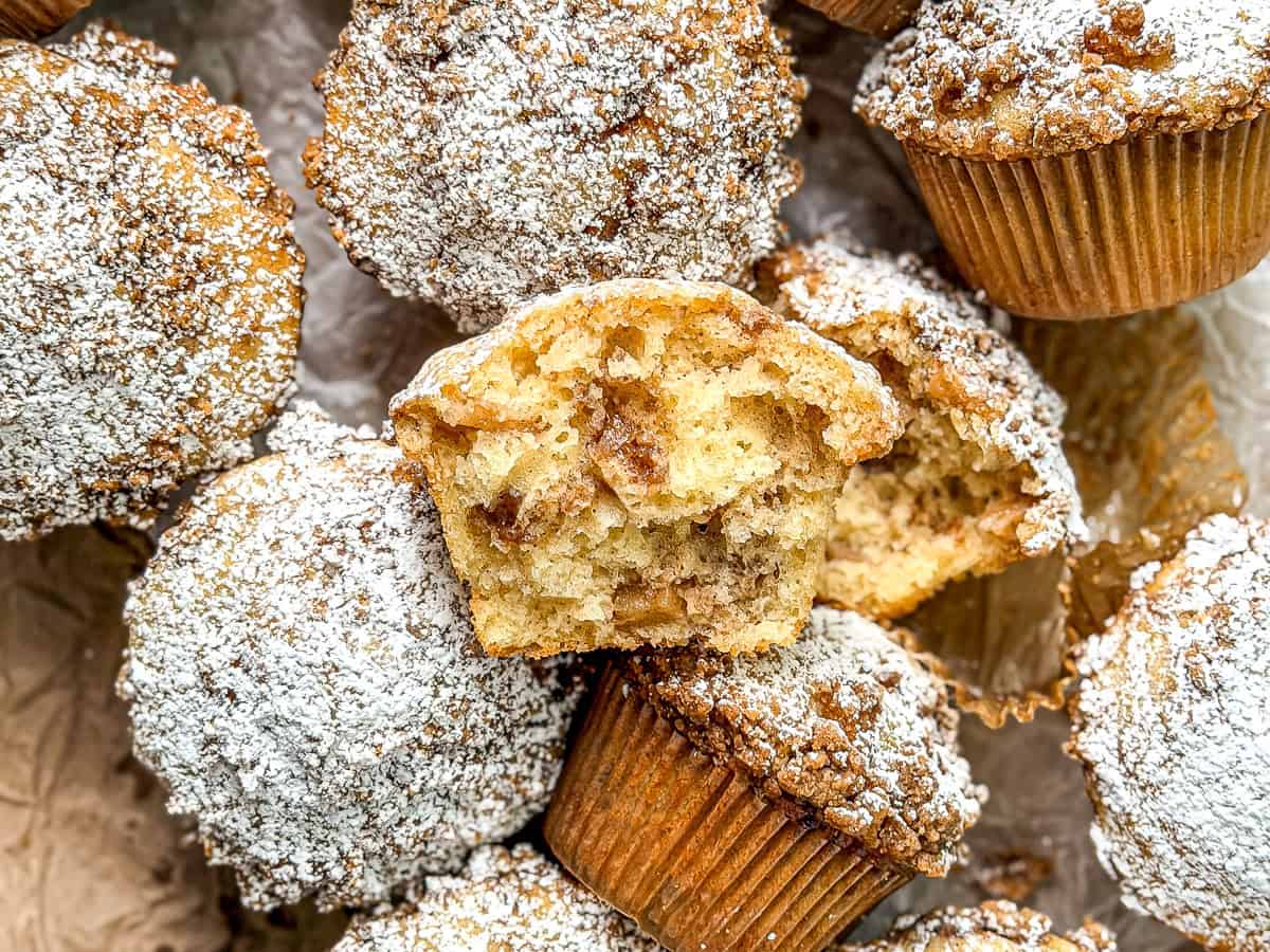 A pile of apple pie muffins, one broken in half to show the interior.