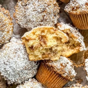 A pile of apple pie muffins, one broken in half to show the interior.