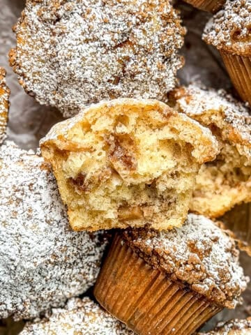 A pile of apple pie muffins, one broken in half to show the interior.