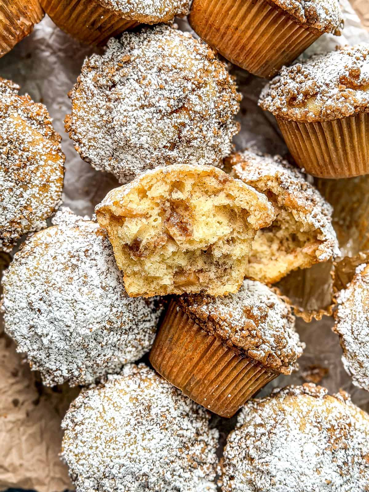 A pile of apple pie muffins, one broken in half to show the interior.
