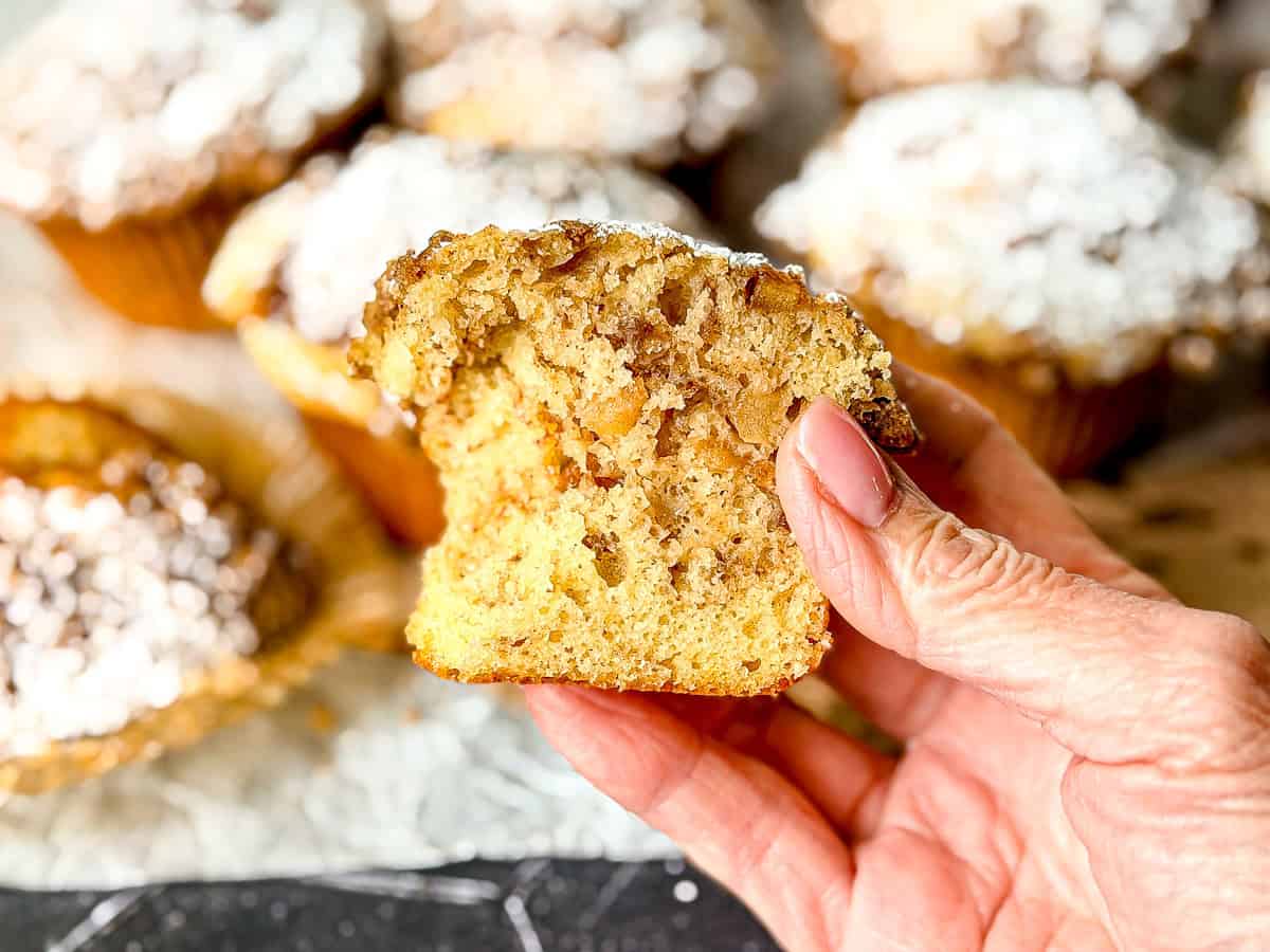 Hand holding half of an apple pie muffin, with a bite taken out.