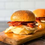 Side view of a bacon egg and cheese sandwich on a poppyseed brioche bun.