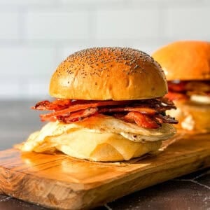 Side view of a bacon egg and cheese sandwich on a poppyseed brioche bun.