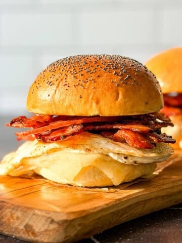 Side view of a bacon egg and cheese sandwich on a poppyseed brioche bun.