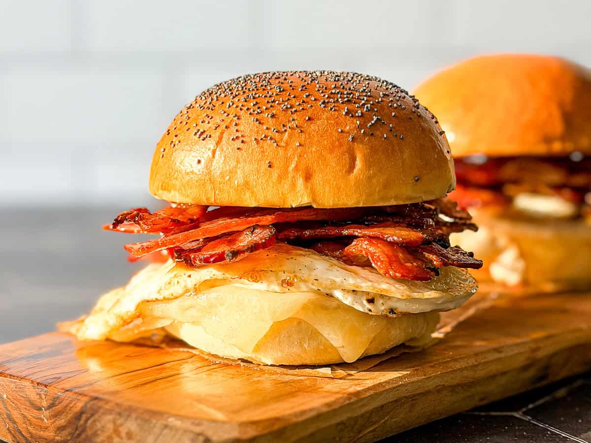 Side view of a bacon egg and cheese sandwich on a poppyseed brioche bun.