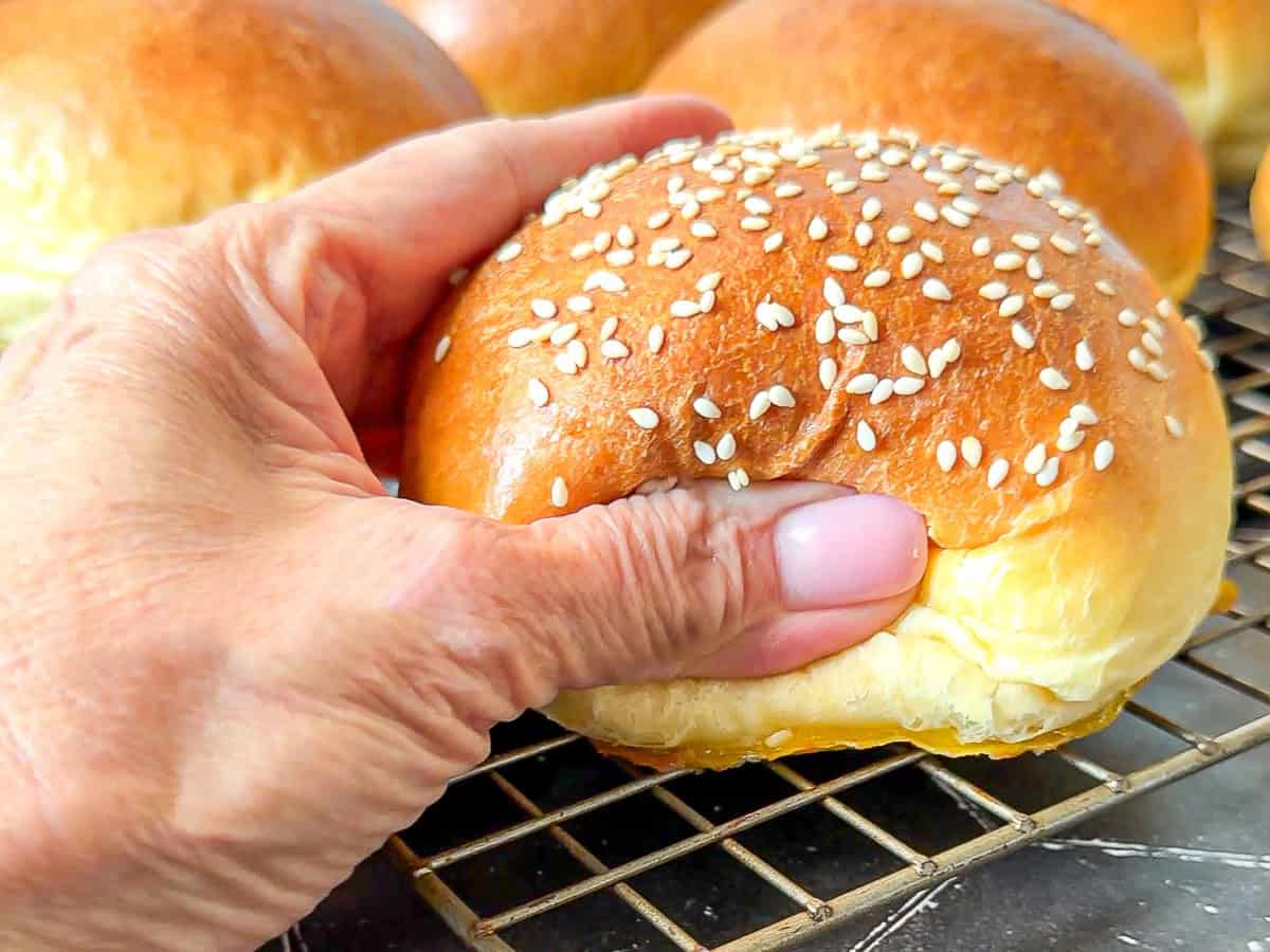 Softly squeezing a brioche bun topped with sesame seeds.