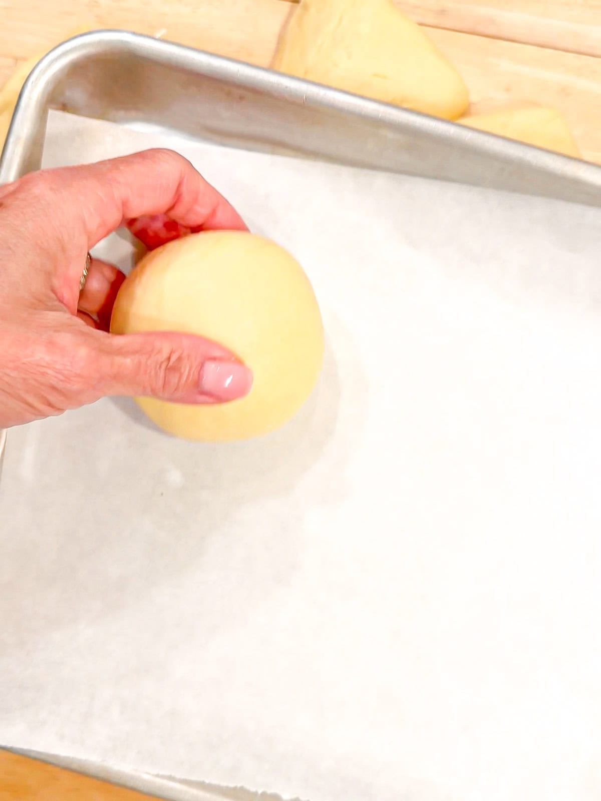 Placing flattened Falls of brioche dough onto a parchment paper lined sheet pan.