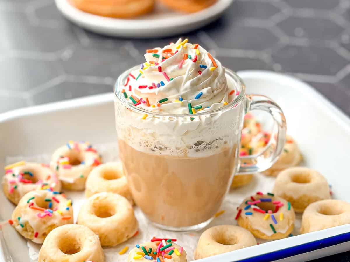 Glazed donut latte in a white tray filled with mini baked donuts.
