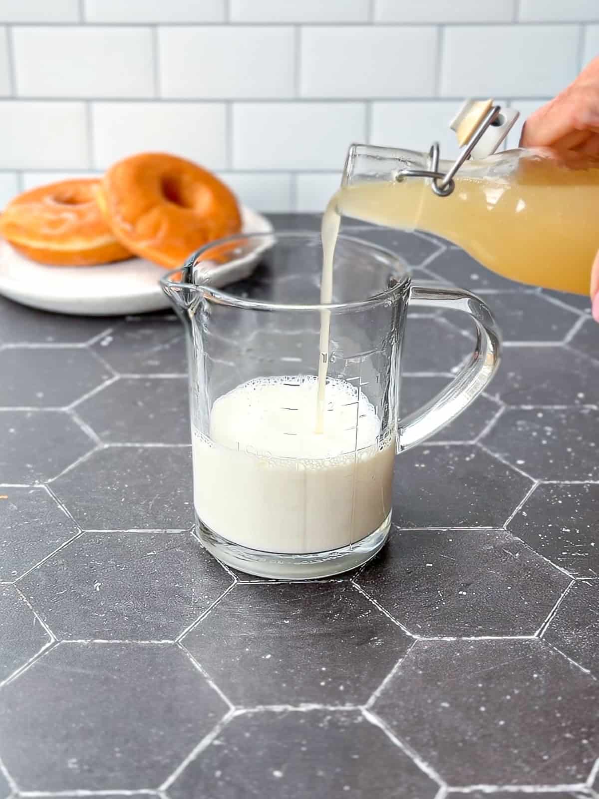 Pouring glazed doughnut simple syrup into hot milk in a measuring cup.