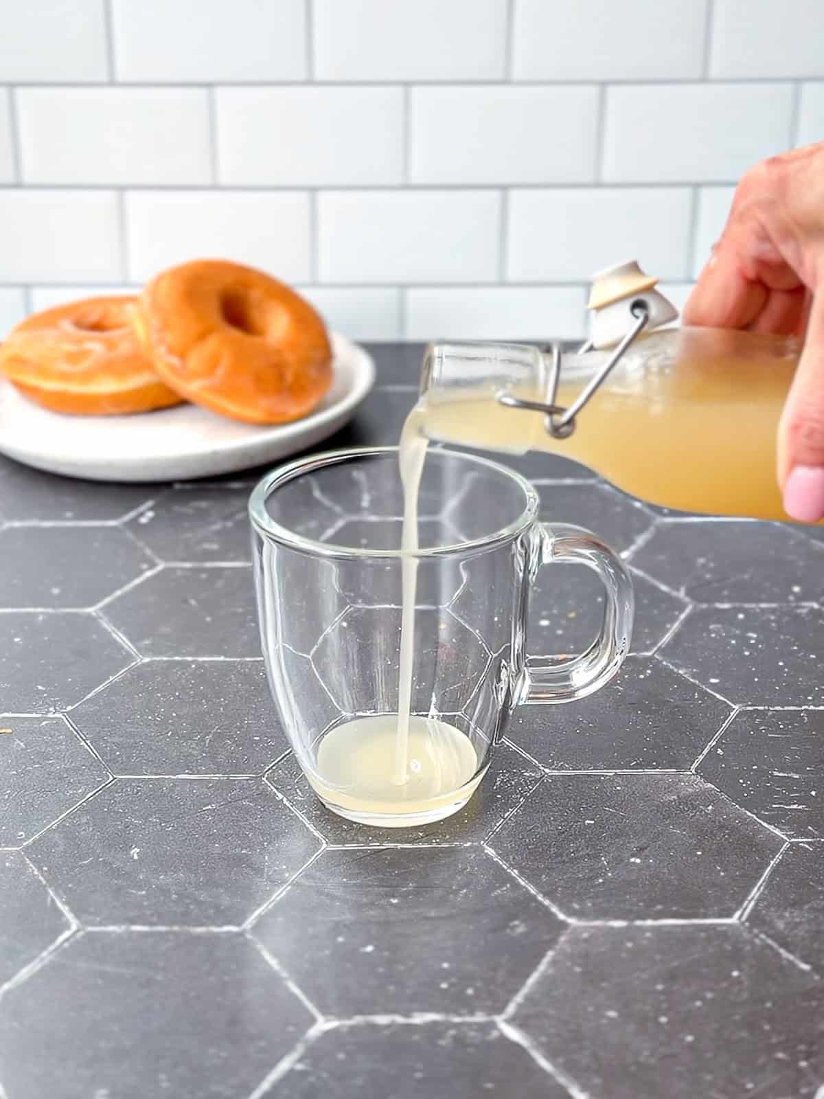 Pouring glazed doughnut simple syrup into a glass mug.