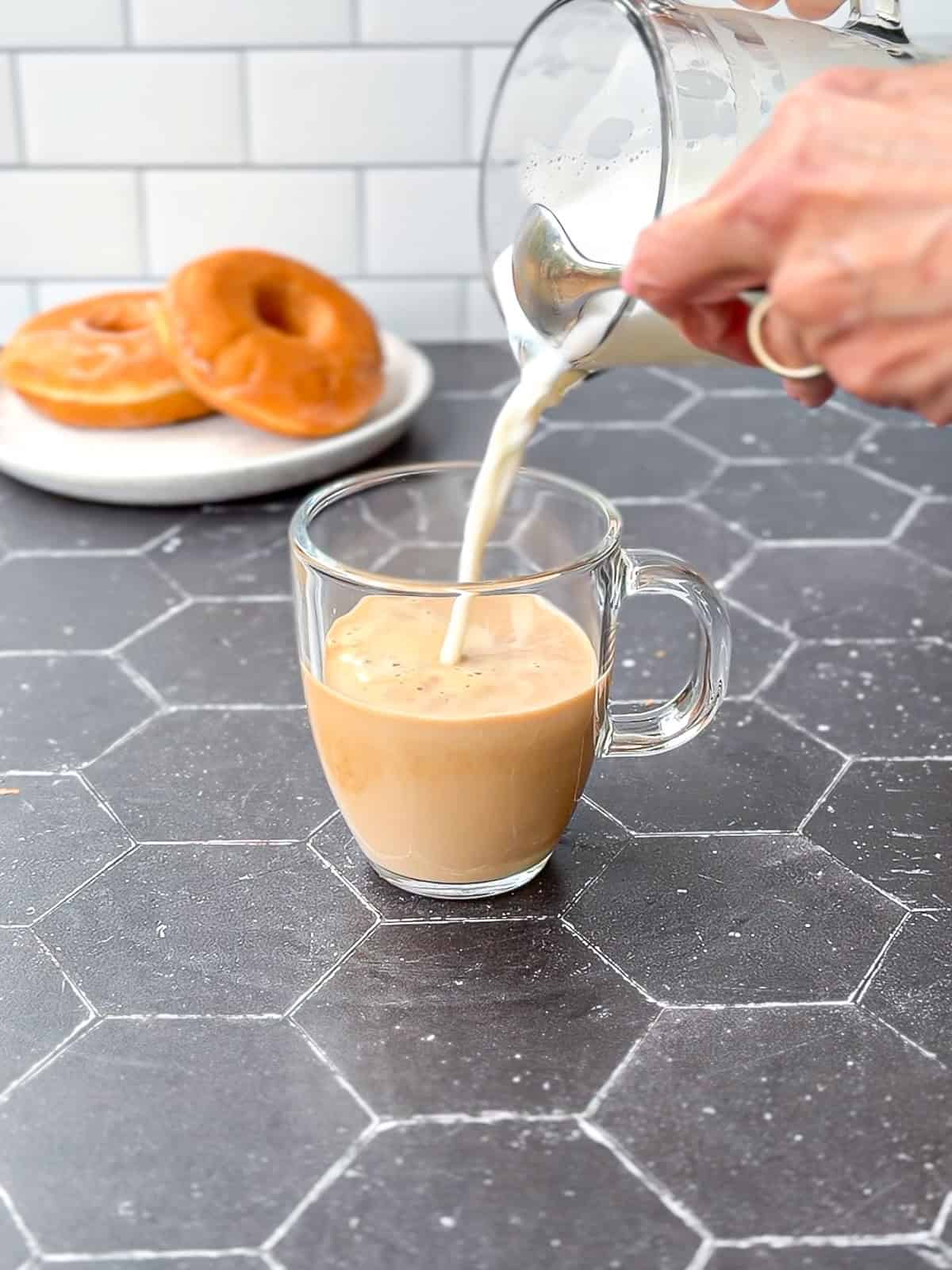 Pouring hot steamed milk into espresso in a glass mug.
