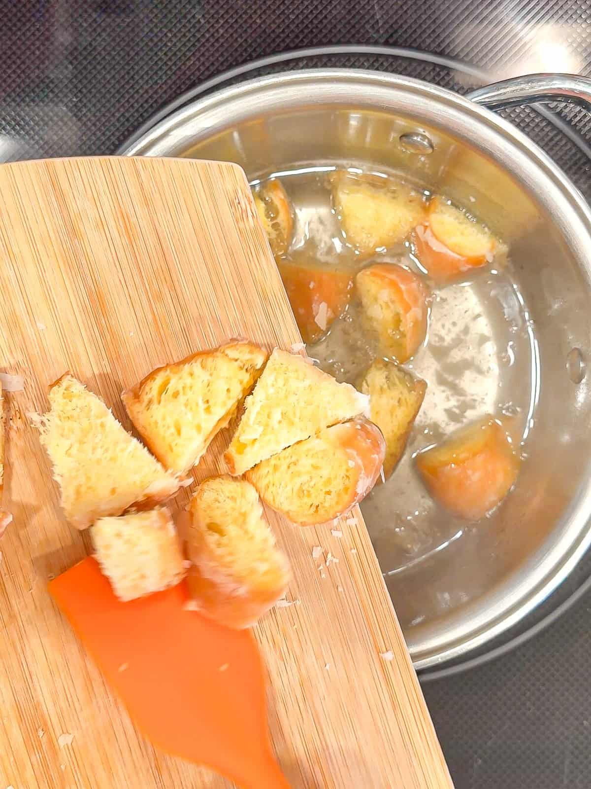 Placing donut pieces into simple syrup in a sauce pan.