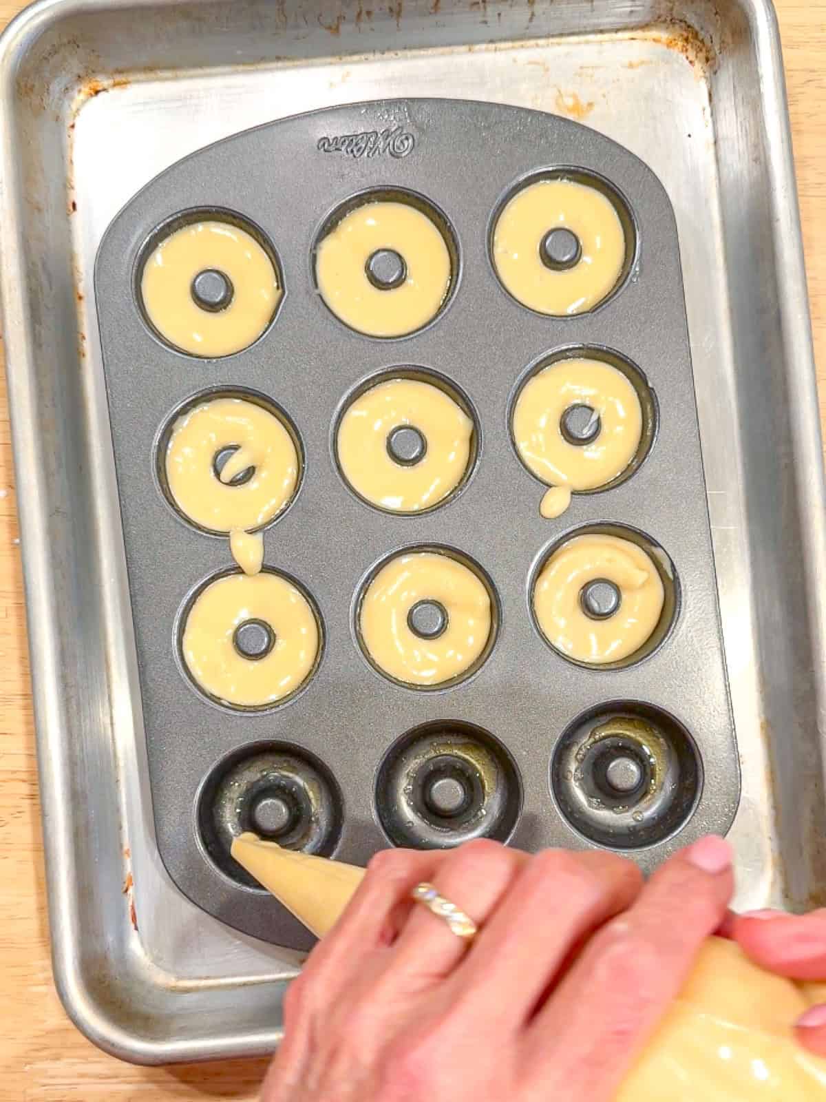 Using a piping bag to distribute donut batter in a mini donut pan.