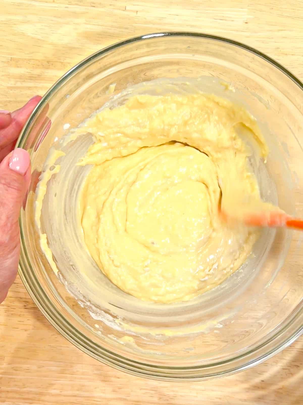 Mixing donut batter in a glass bowl.