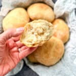 Hand holding a torn open bread roll showing the fluffy interior.