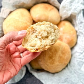 Hand holding a torn open bread roll showing the fluffy interior.