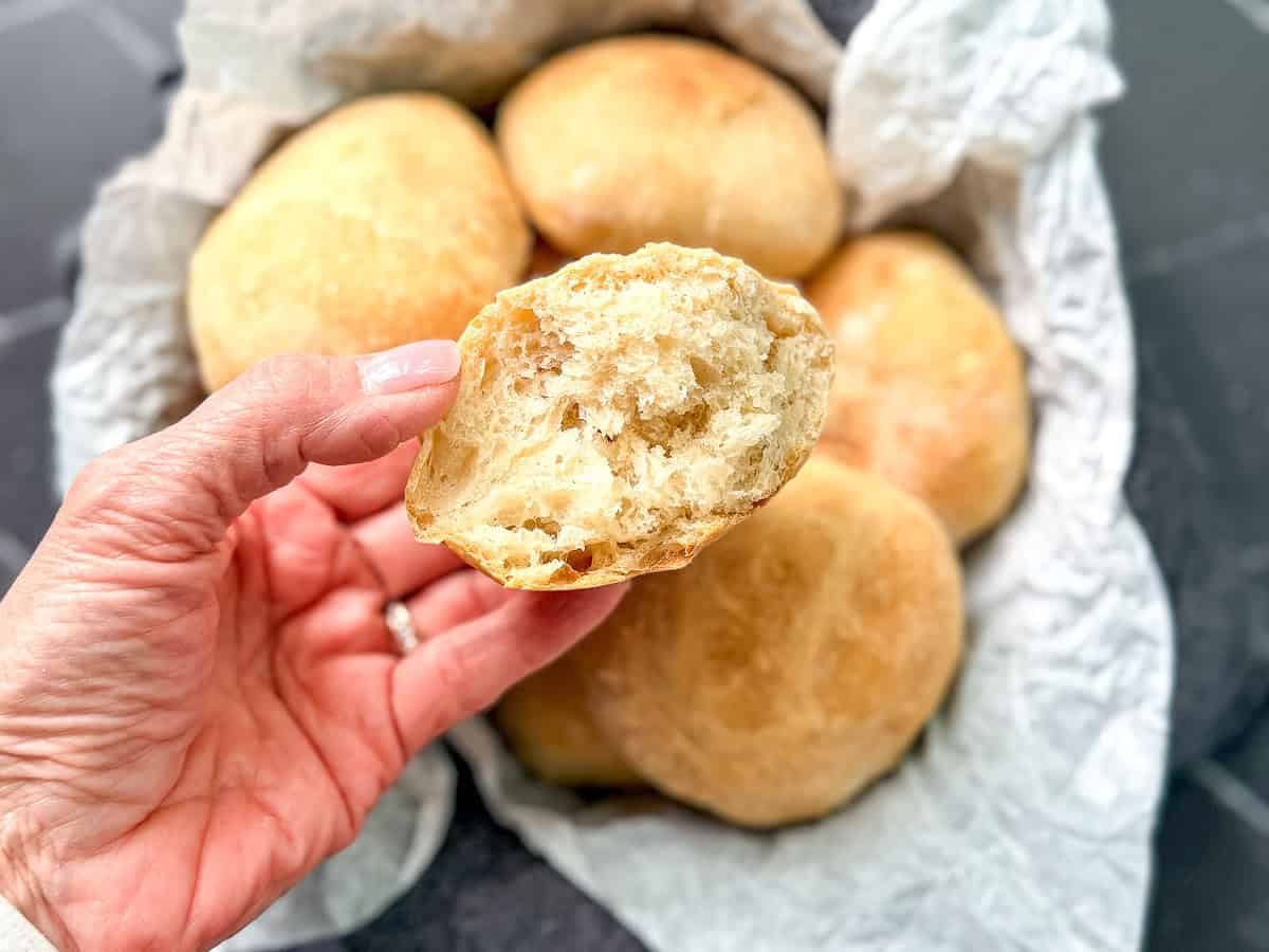 Hand holding a torn open bread roll showing the fluffy interior.