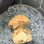 Pinterest image of a bread roll with butter and flaky salt on a blue floral plate.
