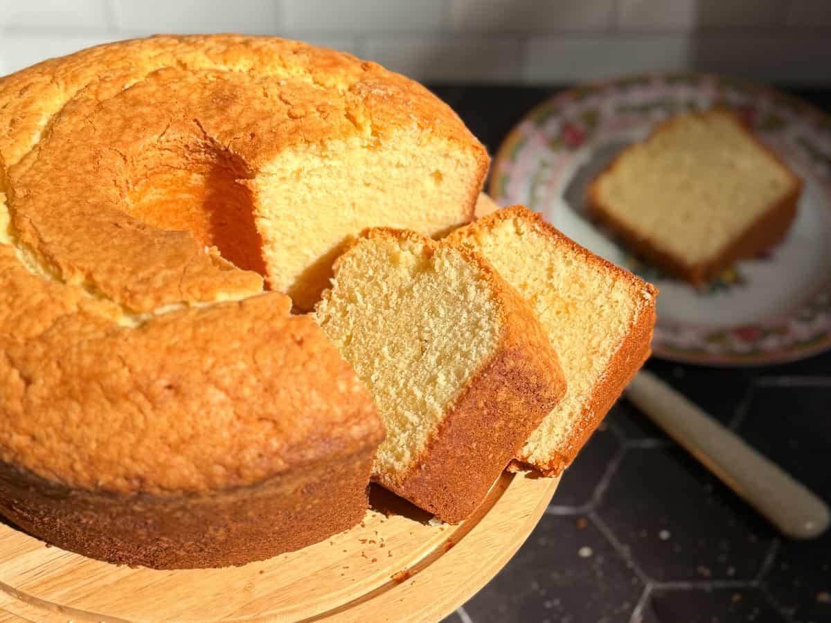 Slices of pound cake on a cake stand with a slice on a plate in the background.