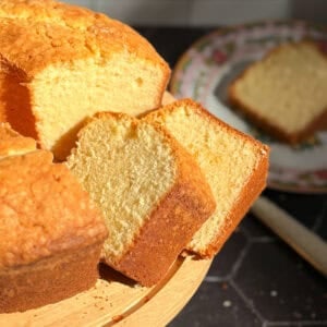 Slices of pound cake on a cake stand with a slice on a plate in the background.