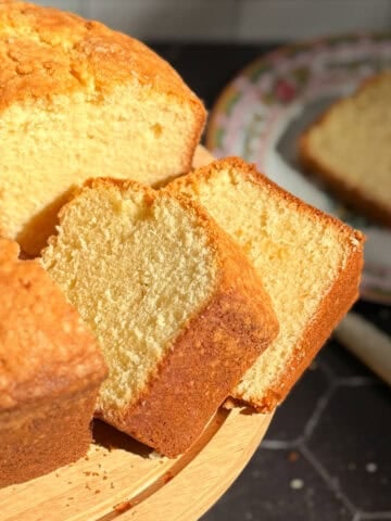 Slices of pound cake on a cake stand with a slice on a plate in the background.