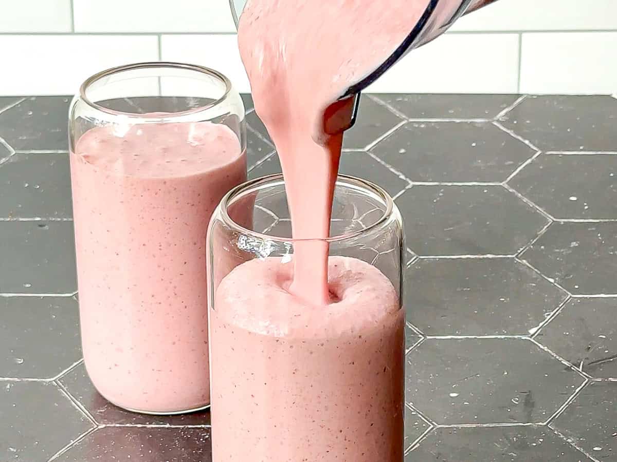 Pouring a strawberry banana smoothie into a tall glass.