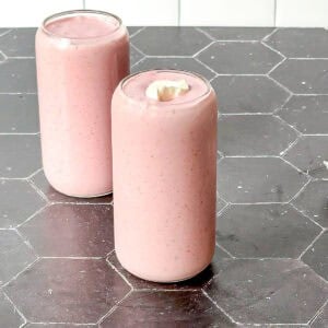 Two strawberry banana smoothies with dollop of yogurt on a black counter with a white backdrop.