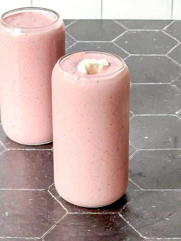 Two strawberry banana smoothies with dollop of yogurt on a black counter with a white backdrop.