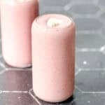Two strawberry banana smoothies with dollop of yogurt on a black counter with a white backdrop.