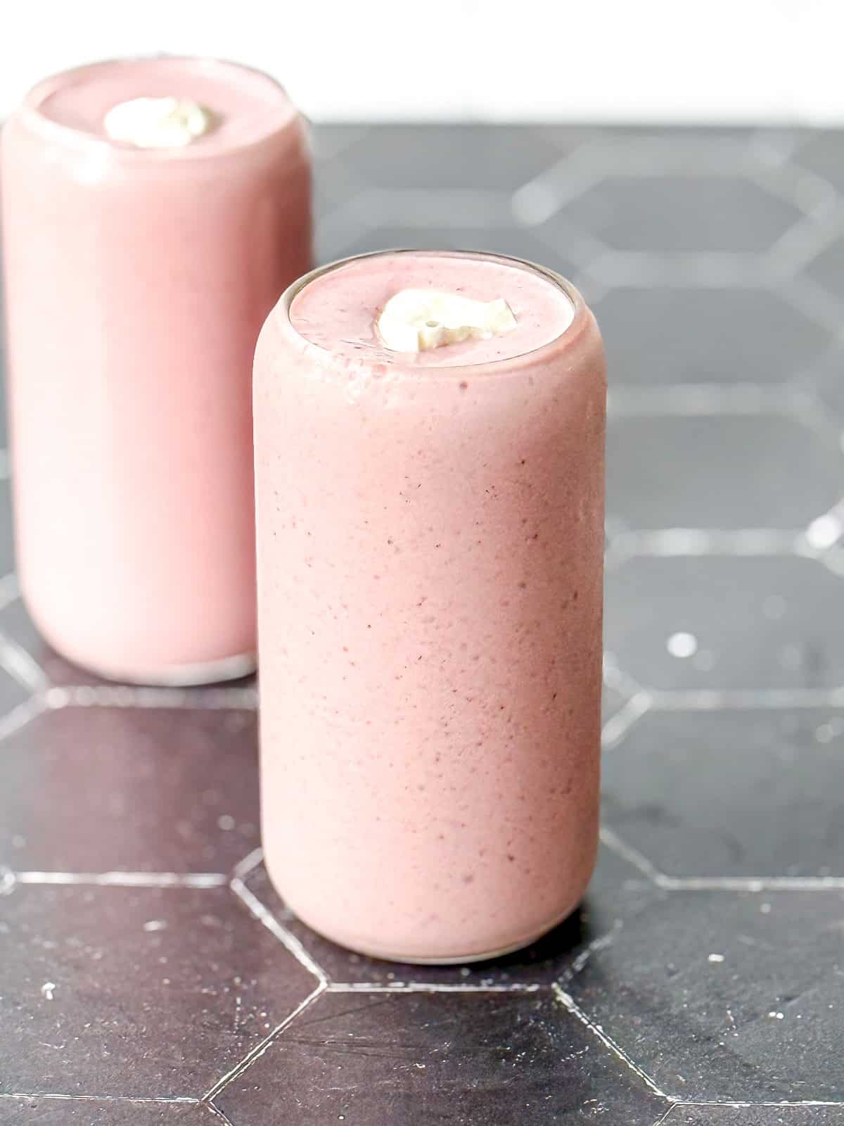 Two strawberry banana smoothies with dollop of yogurt on a black counter with a white backdrop.