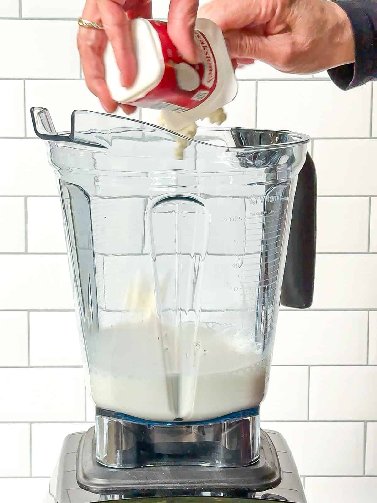 Scooping cottage cheese into milk in a blender.