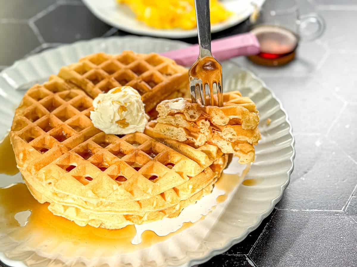 Waffles with butter and syrup on a scalloped plate.