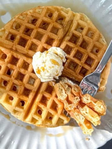 Waffles with butter and syrup on a scalloped plate.