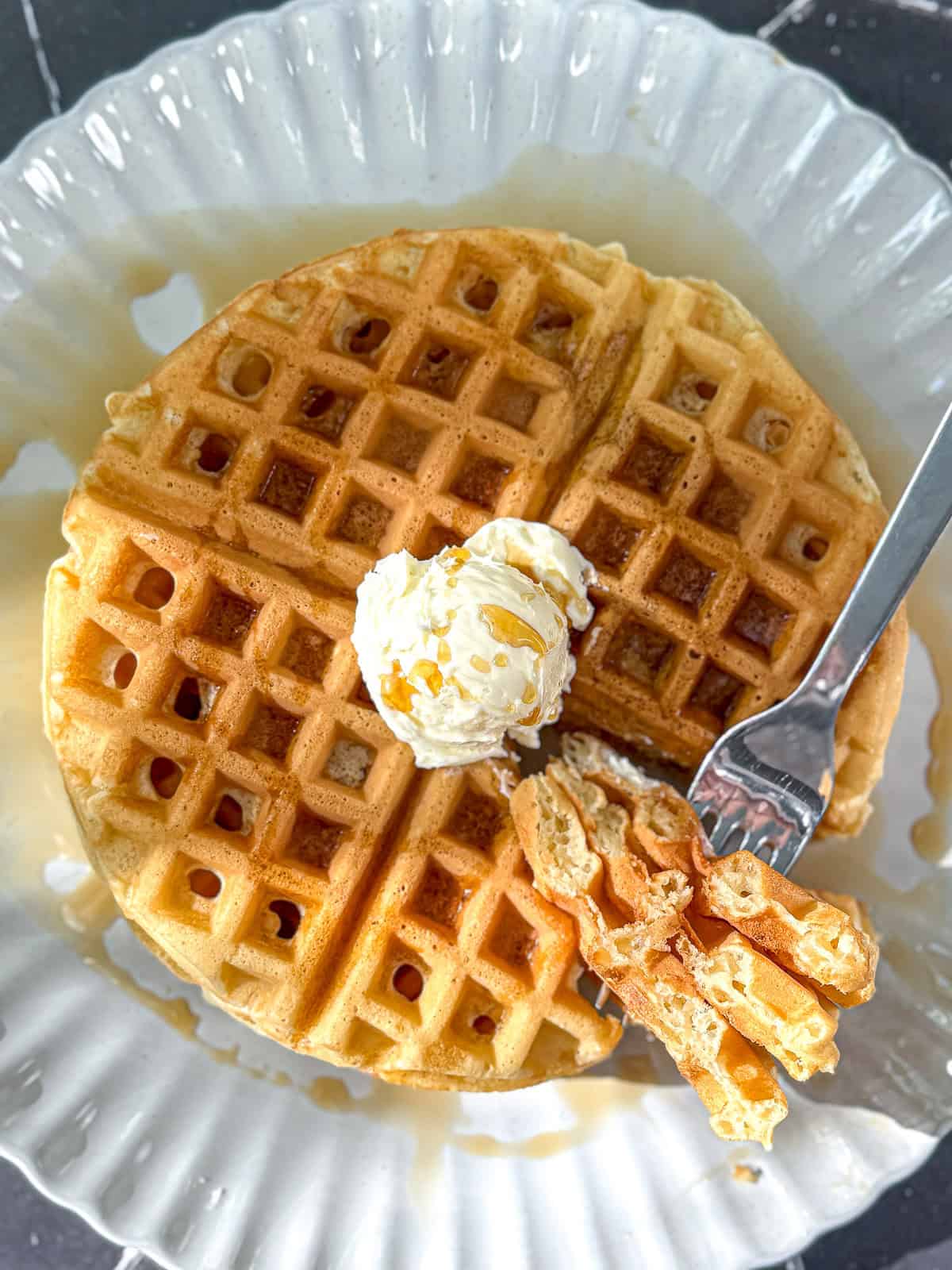 Waffles with butter and syrup on a scalloped plate.