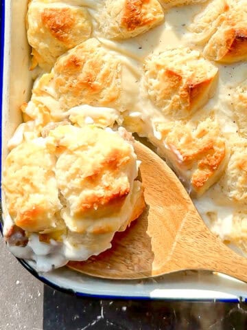 Wooden spoon holding biscuits and gravy casserole.
