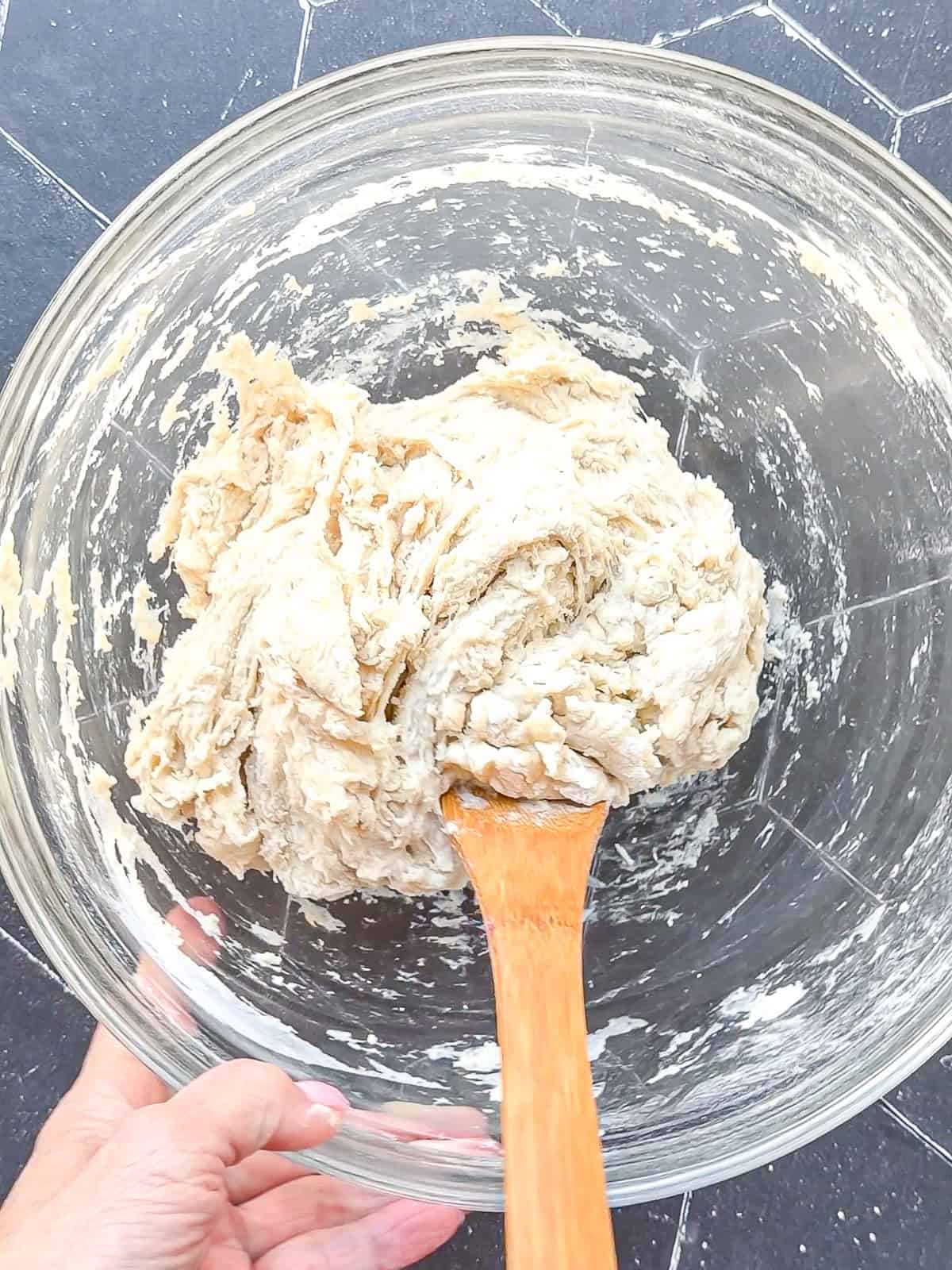 Mixed bread dough in a glass bowl with a wooden spoon.