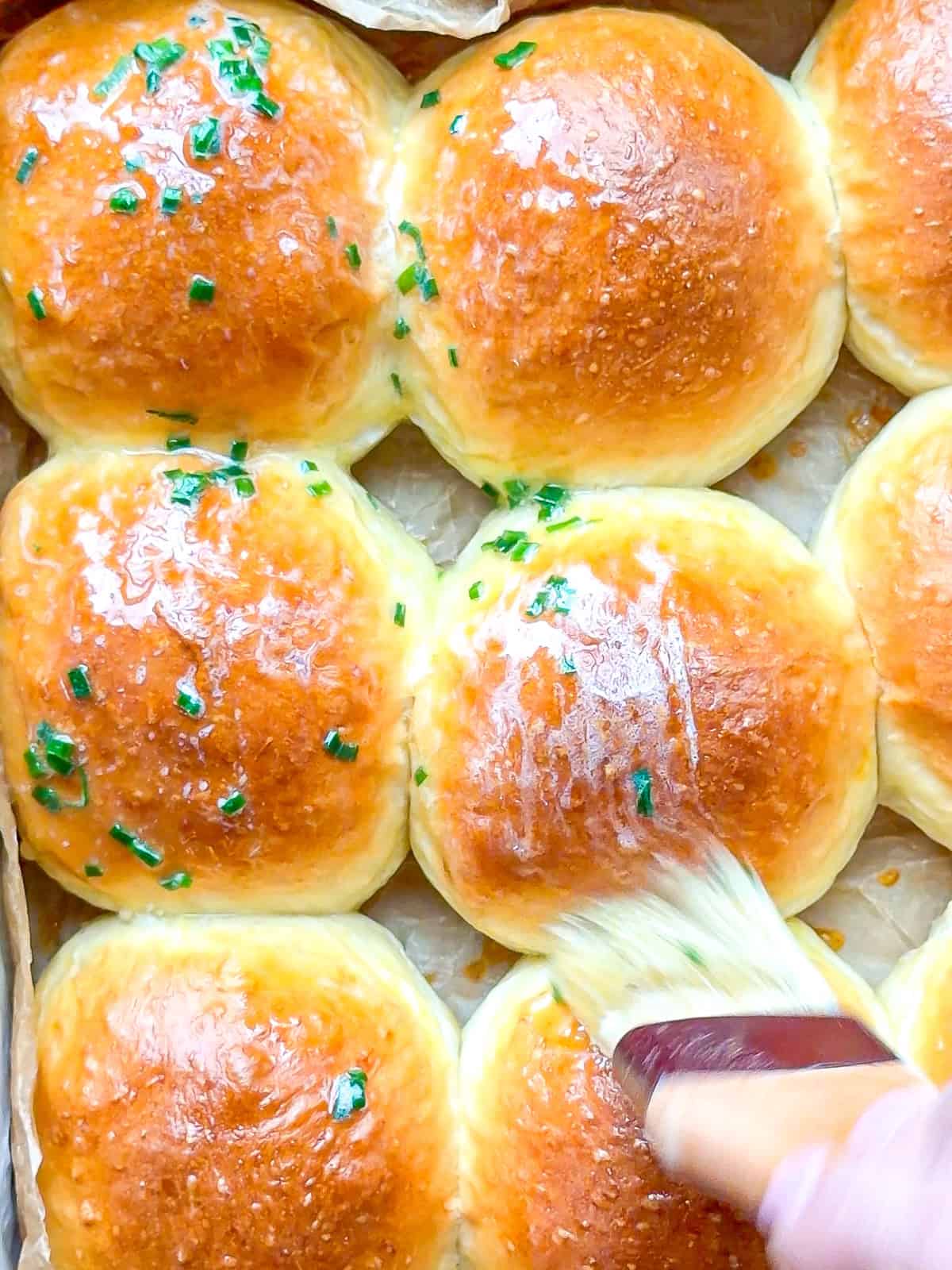 Brushing chive butter on warm dinner rolls.