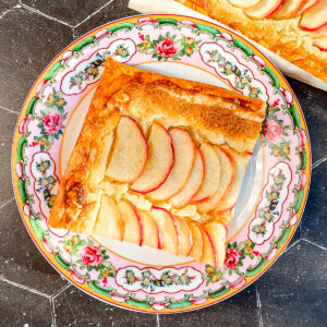 Slice of apple frangipane tart on a floral plate.