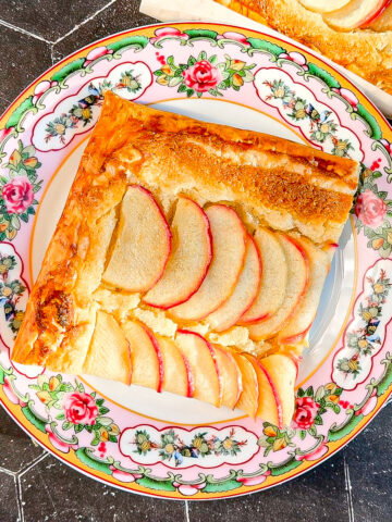 Slice of apple frangipane tart on a floral plate.