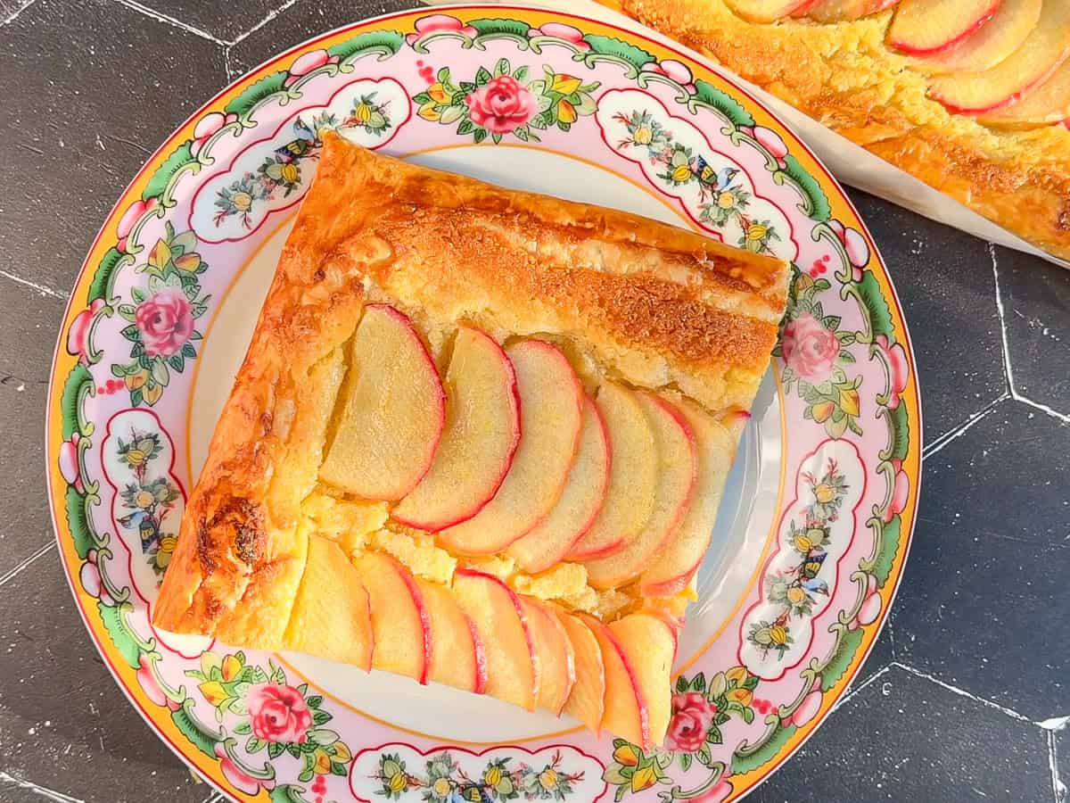 Slice of apple frangipane tart on a floral plate.