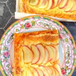 Slice of apple frangipane tart on a floral plate.