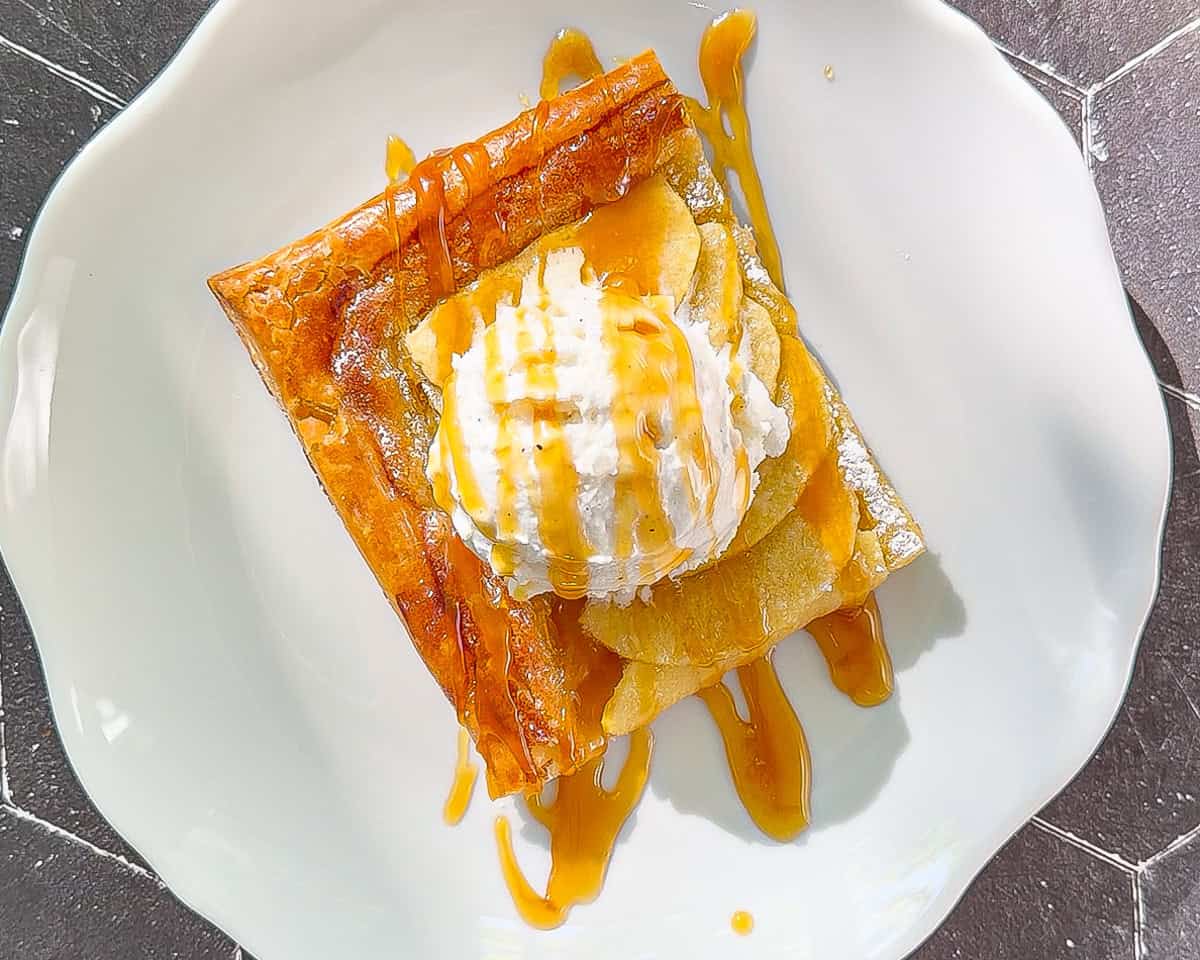 A slice of frangipane tart on a white plate with a scoop of ice cream and a drizzle of salted caramel.