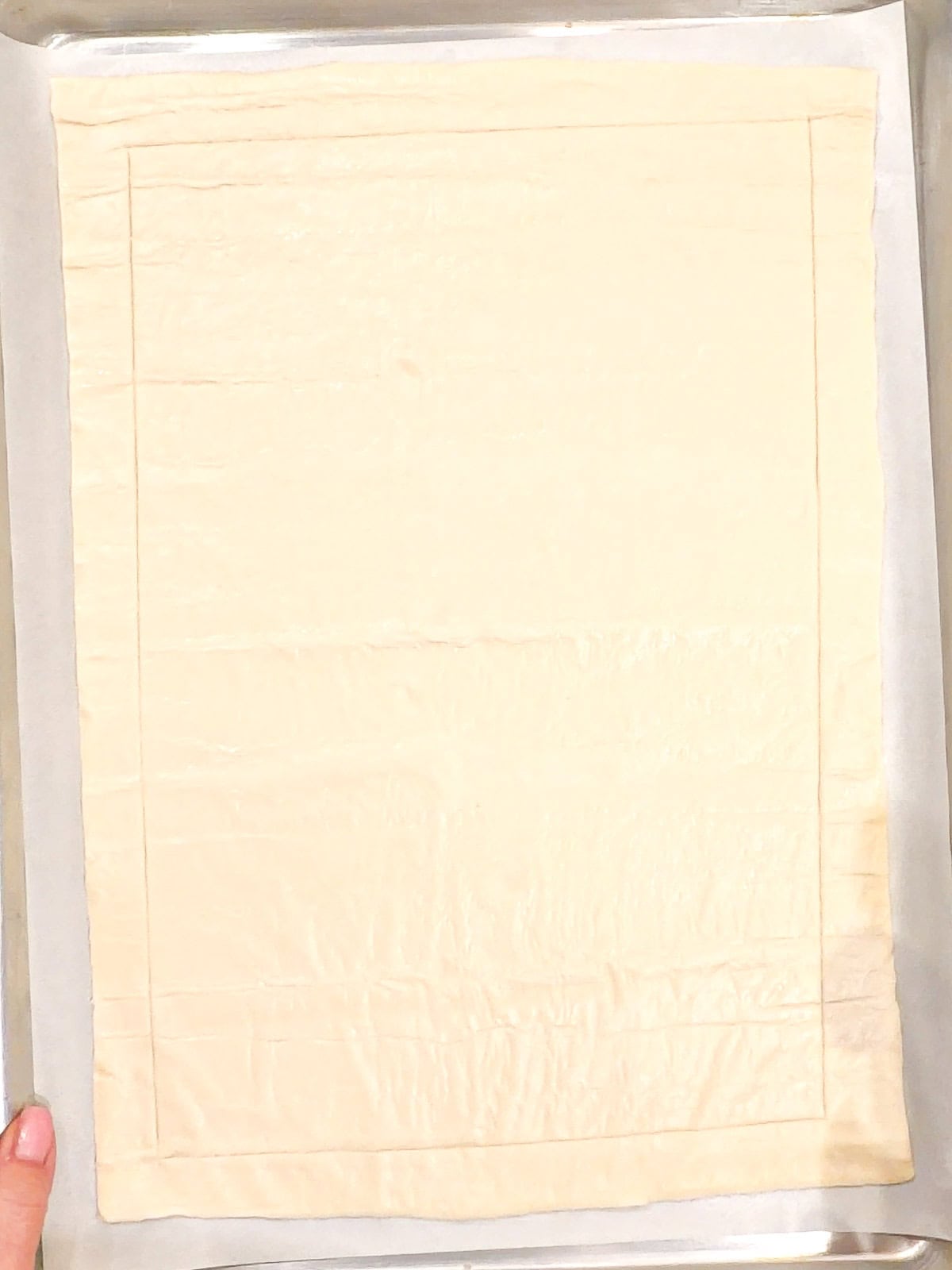 Sheet of puff pastry showing a line scored around the edge.