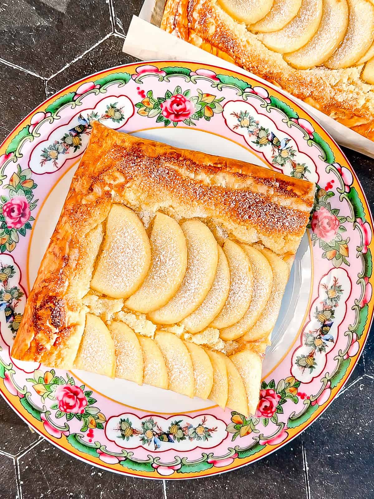 A slice of apple frangipane tart on a pink floral plate.