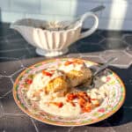 Biscuits with bacon and gravy on a floral plate with a gravy boat in the background.