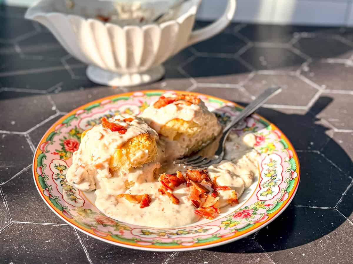 Biscuits with bacon and gravy on a floral plate.
