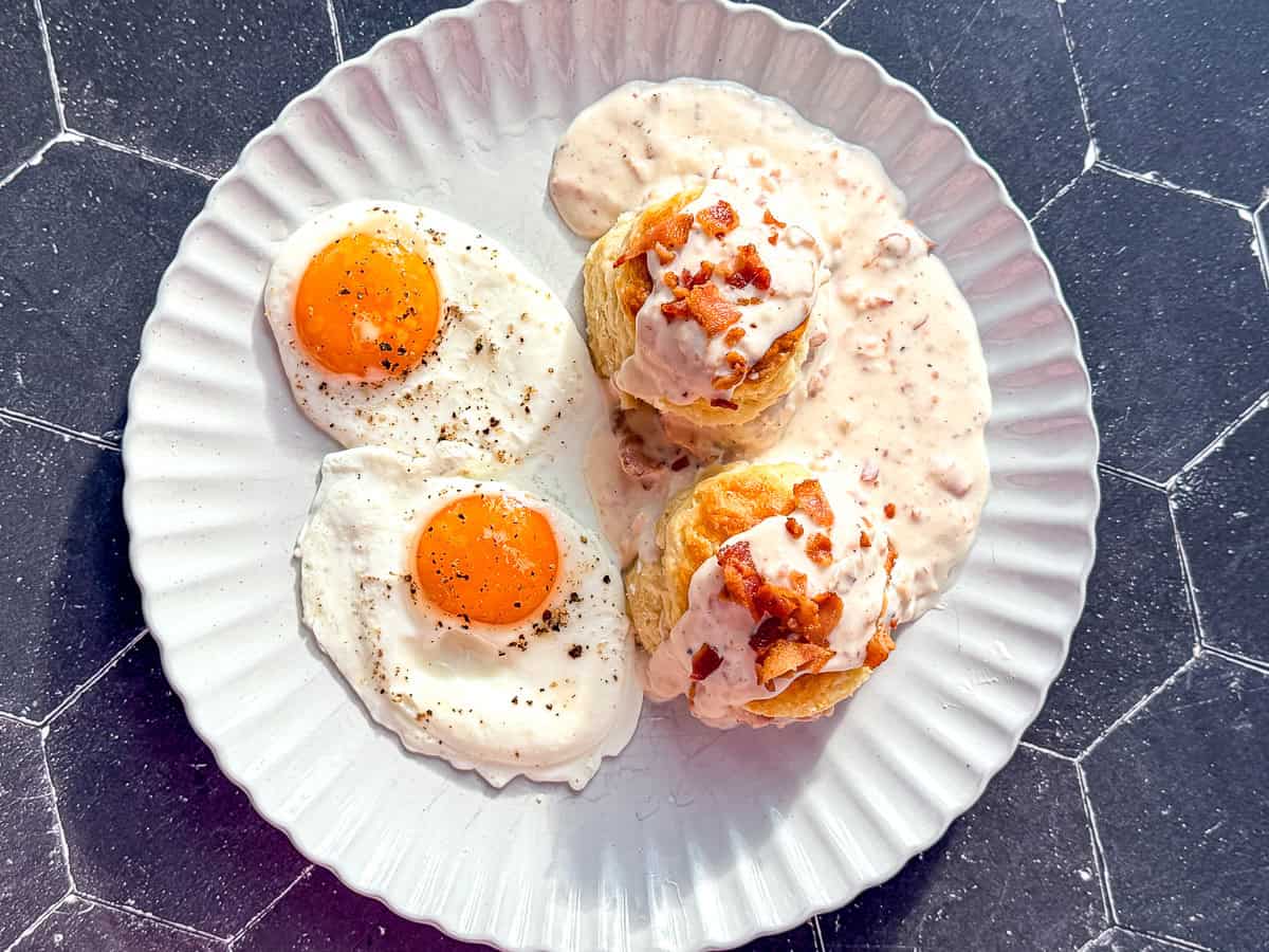 Biscuits with bacon gravy next to two sunny side up eggs.