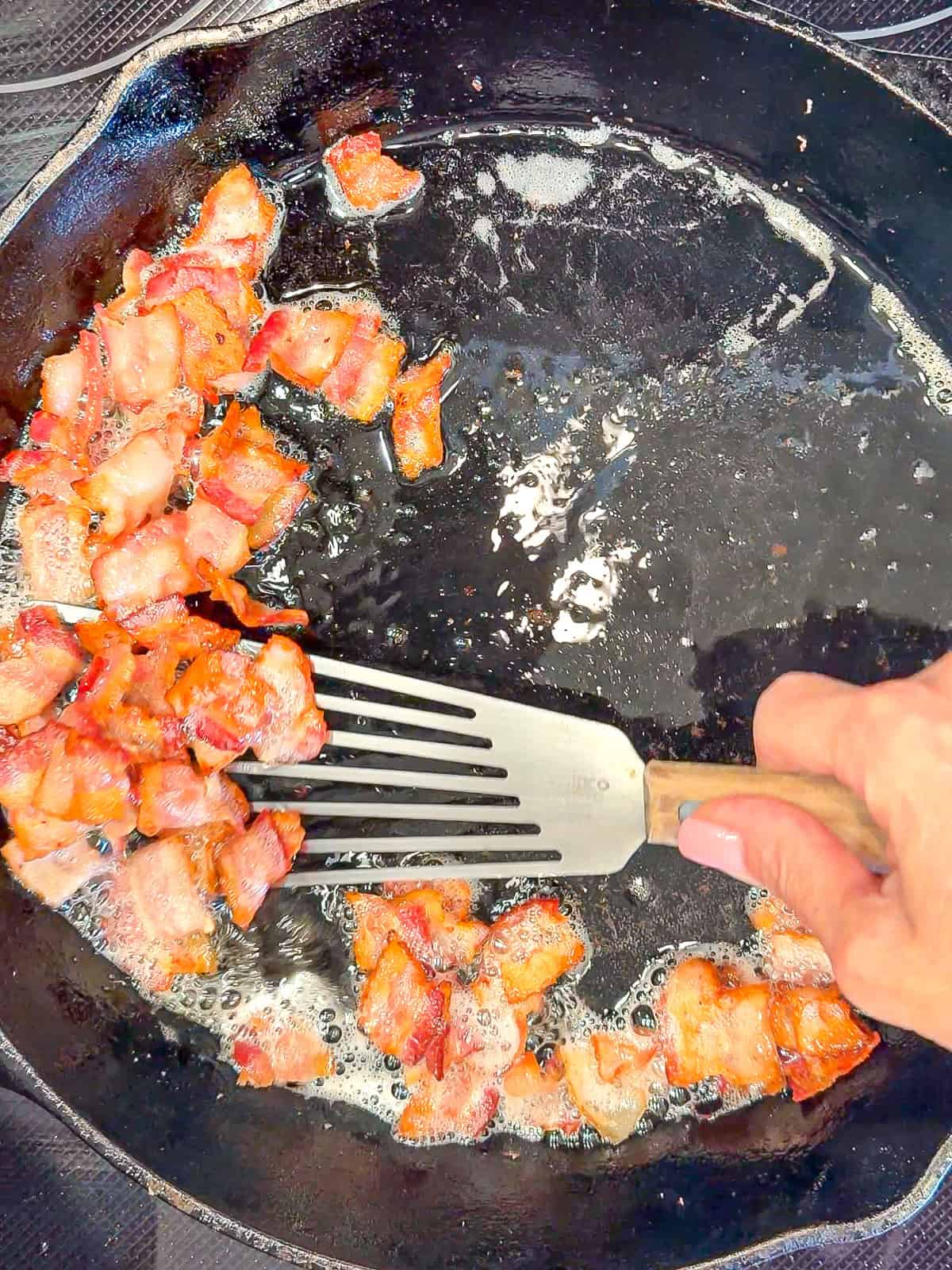 Taking bacon out of a cast-iron pan with a slotted spatula.