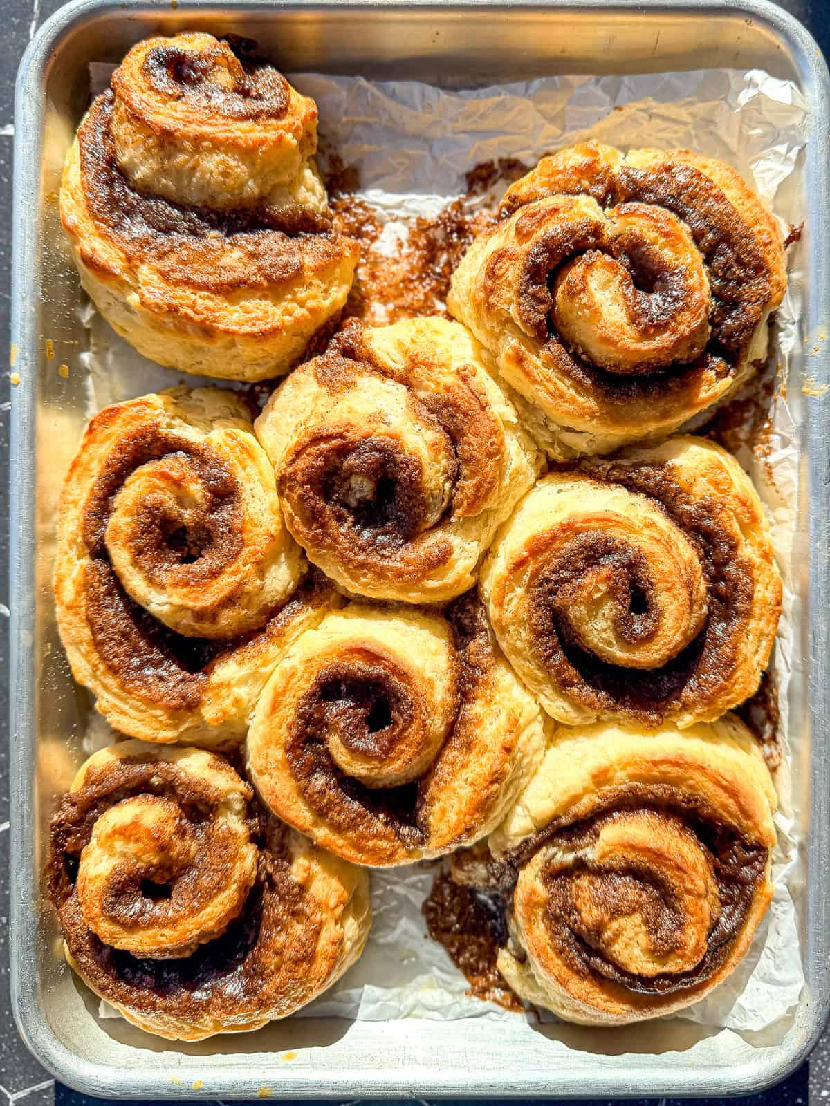 Unfrosted cinnamon rolls on a parchment paper lined sheet pan.