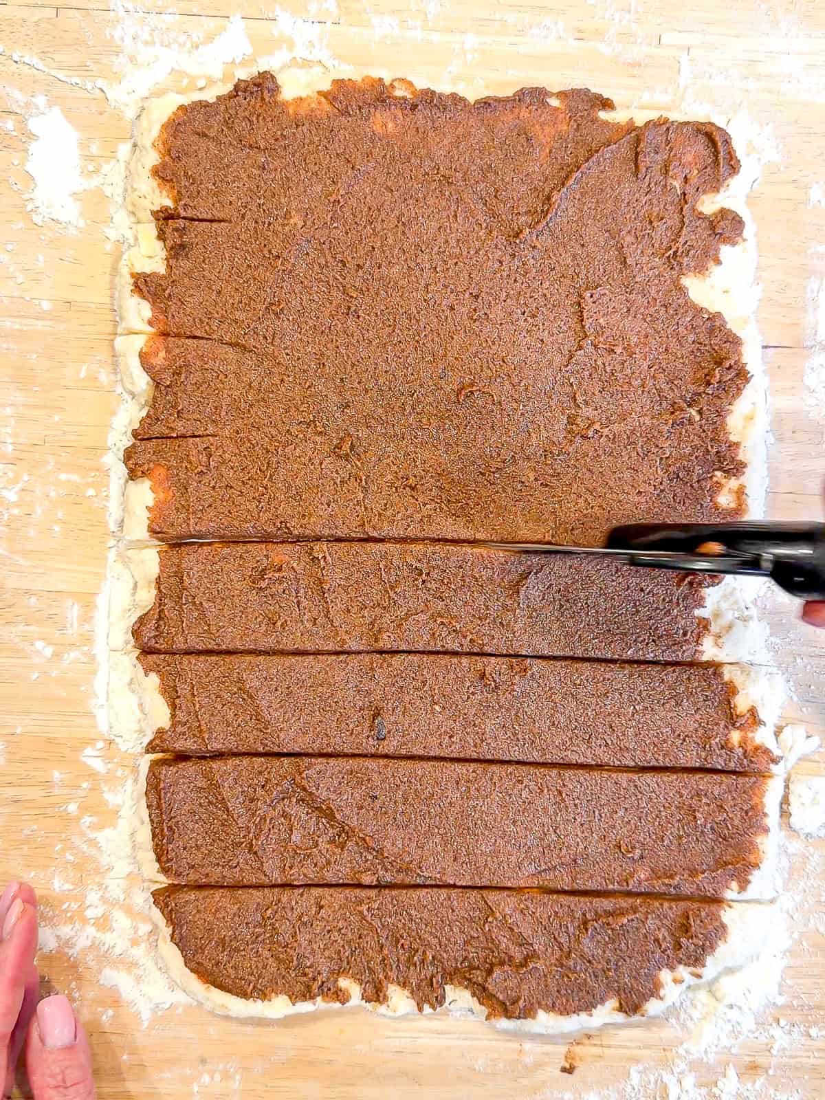 Cutting cinnamon sugar covered biscuit dough with a pizza cutter.